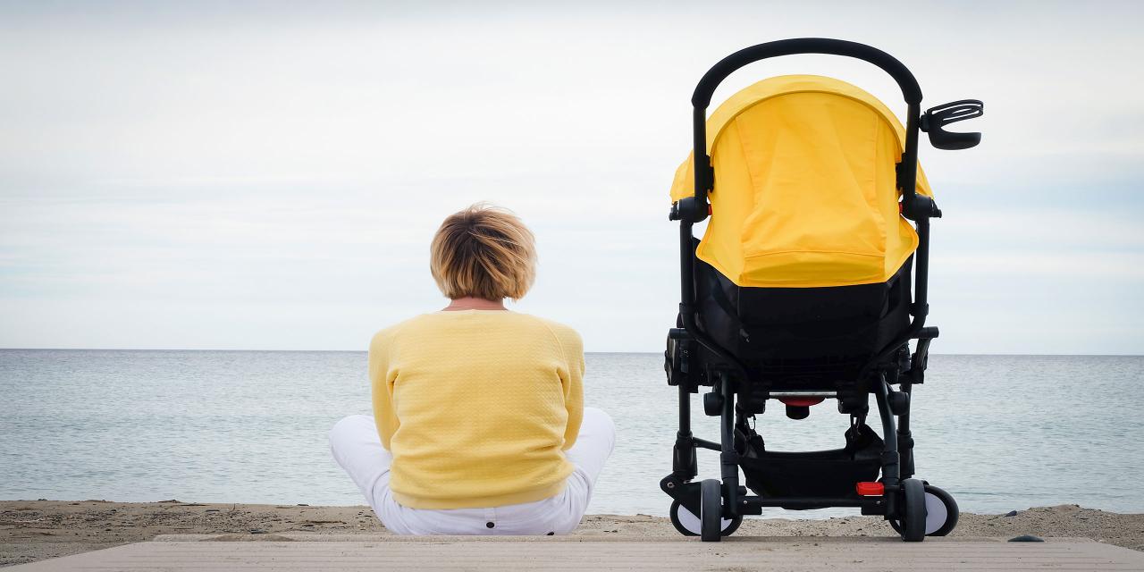 Frau sitzt am Strand und blickt aufs Meer. Gelb-schwarzer Buggy steht links neben ihr.