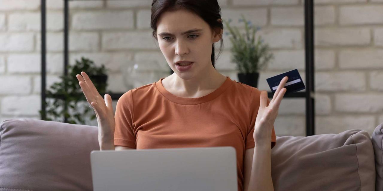 Enttäuschte Frau mit Kreidtkarte in der Hand vor einem Laptop