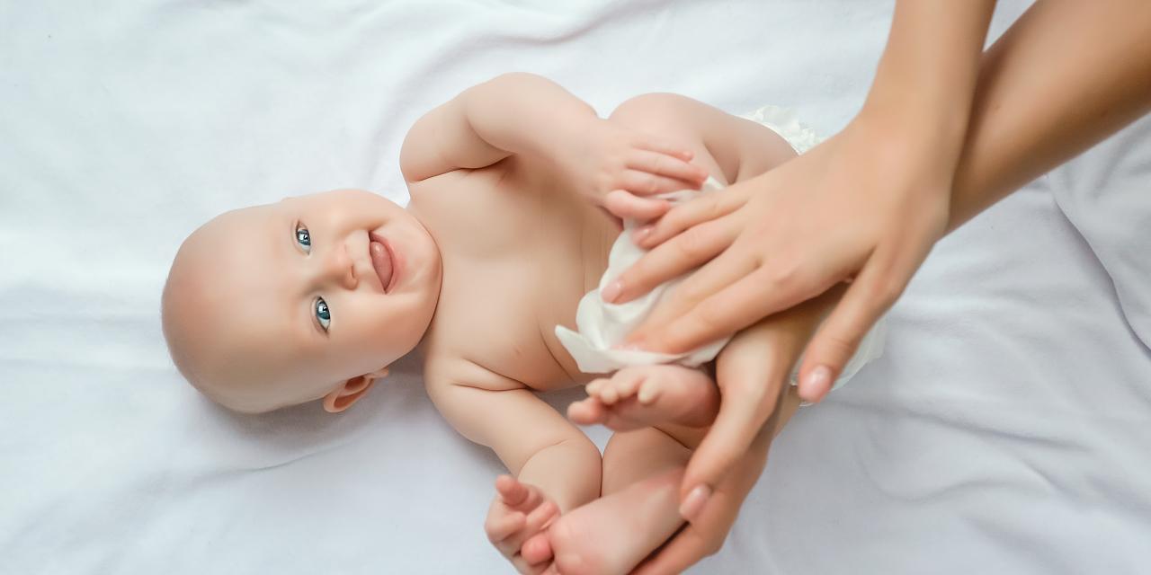Baby liegt am Rücken, Frau greift nach der Windel