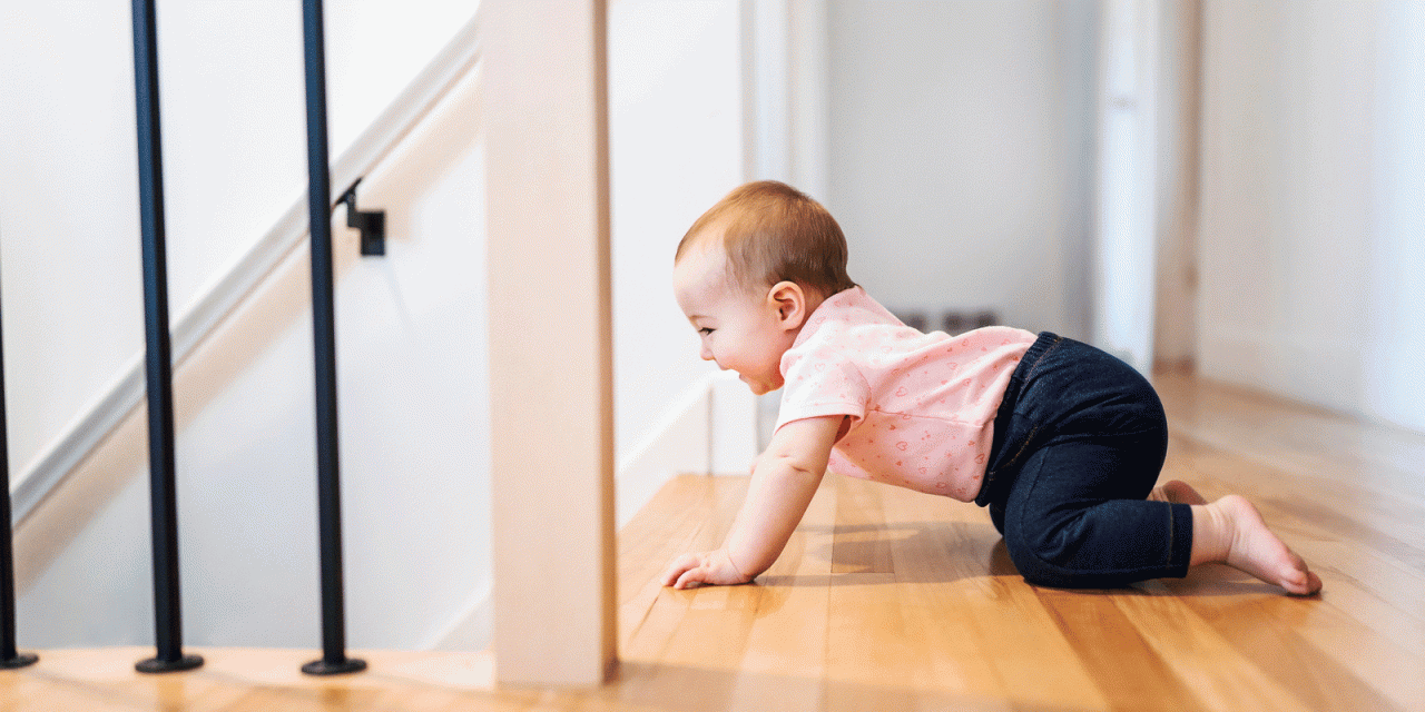 Baby mit hellem Leiberl und dunkler Hose krabbelt auf einen steilen ungesicherten Stiegenabgang zu.