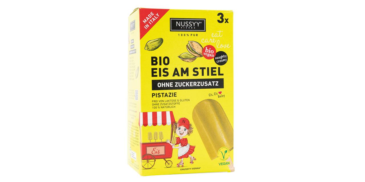 Eine Packung Nussyy Bio Eis am Stiel der Sorte Pistazie in gelb-grüner Kartonverpackung vor weißem Hintergrund. 