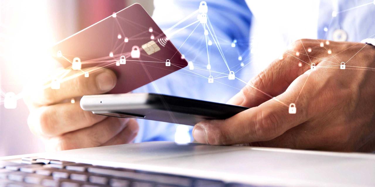 Männerhände halten vor einem Notebook Bankkarte und Smartphone für eine Überweisung