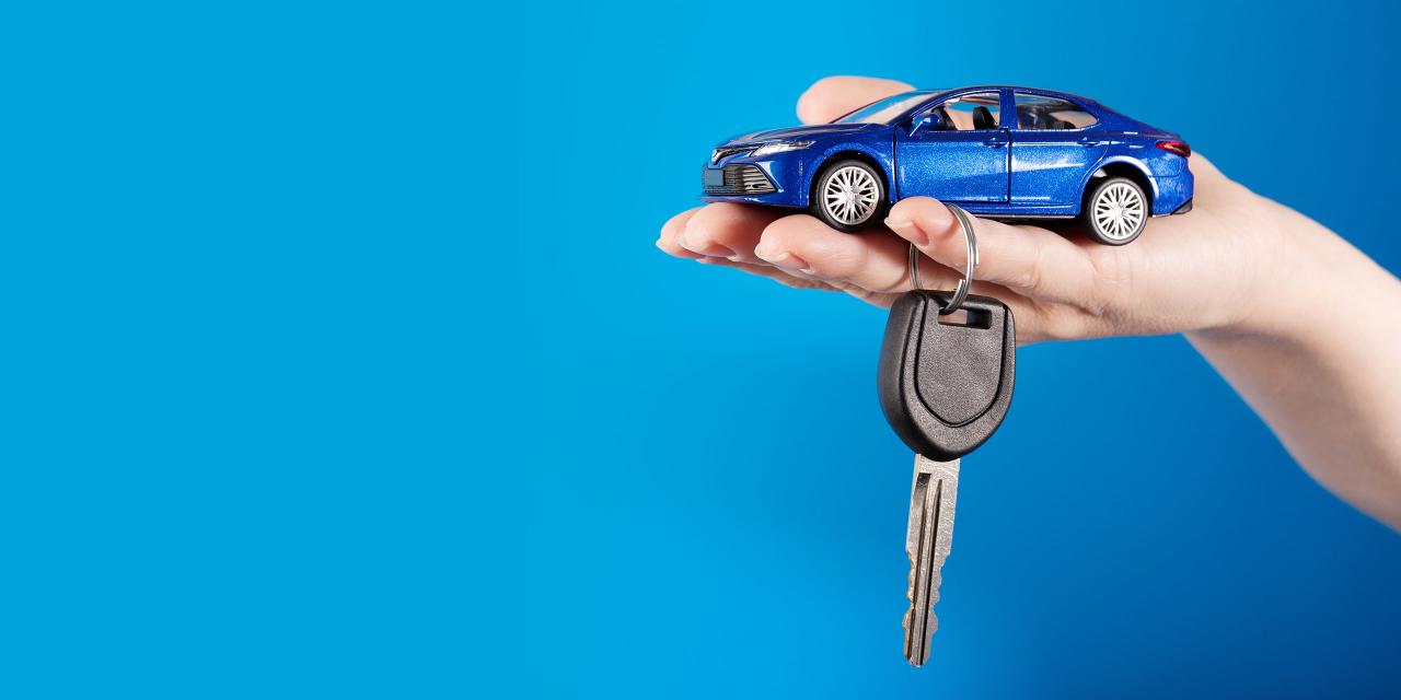 Eine Hand hält ein Miniaturauto samt Autoschlüssel