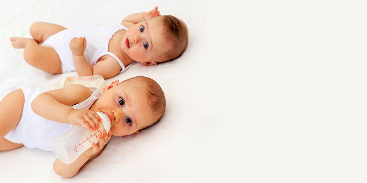 Zwei Babys am Rücken, eines trinkt aus einer Flasche