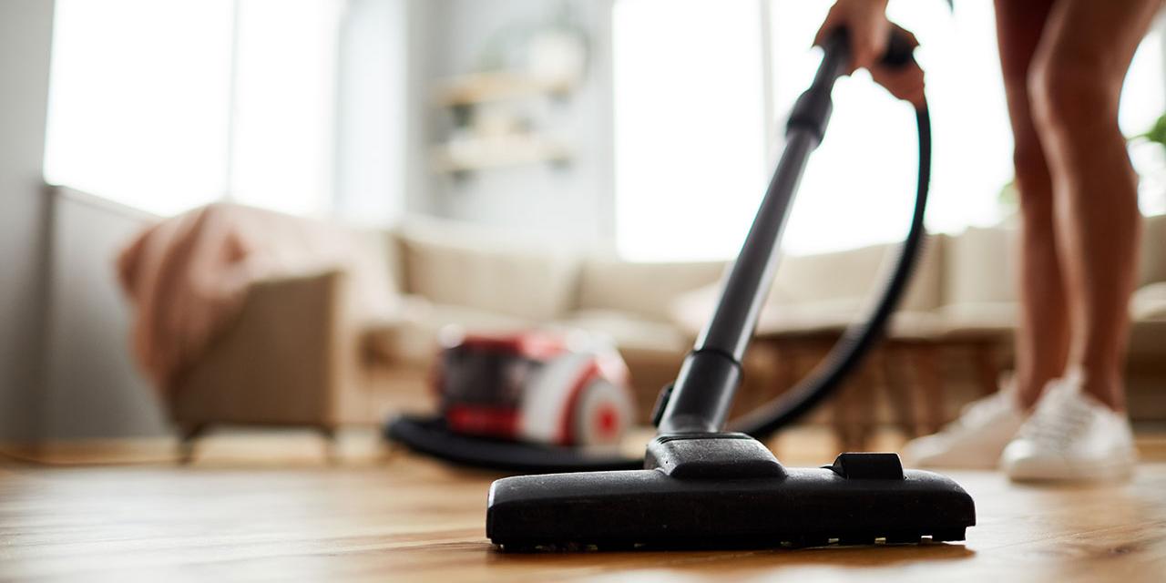 Person in Turnschuhe führt Staubsauger über Parkettboden