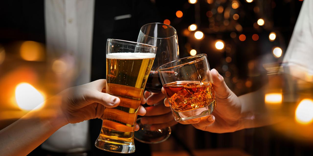 Weihnachtliche Beleuchtung, Hände mit gefüllten Gläsern stoßen an, Hintergrund Anzugträger, bunte Weihnachtsbeleuchtung.