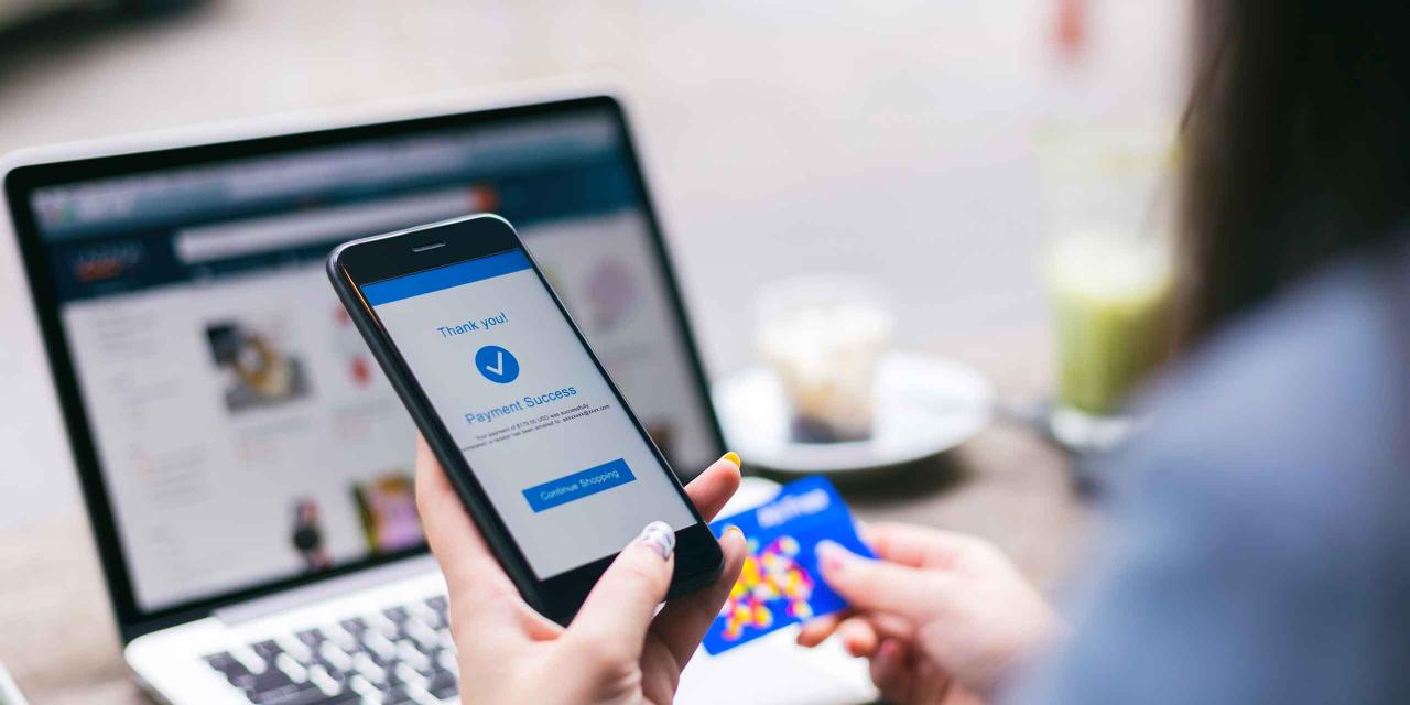 Frau beim Online-Shopping vor dem Notebook mit Handy und Kreditkarte