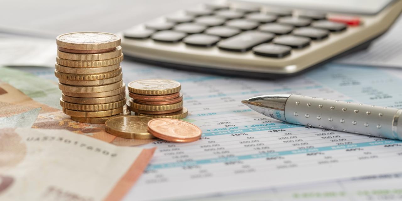 Auf einem Tisch liegen Geld, ein Taschenrechner, ein Stift und ein Zettel mit vielen Zahlen darauf