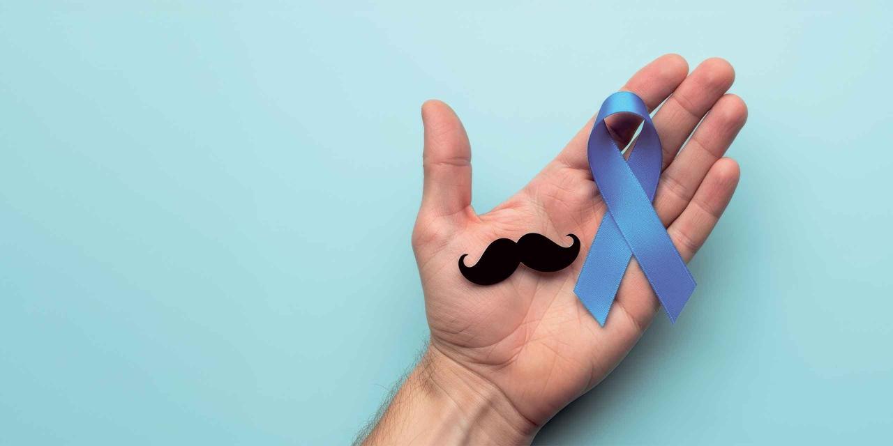 Auf einer Männerhand liegt ein Papier-Schnurrbart und ein Blue-Ribbon