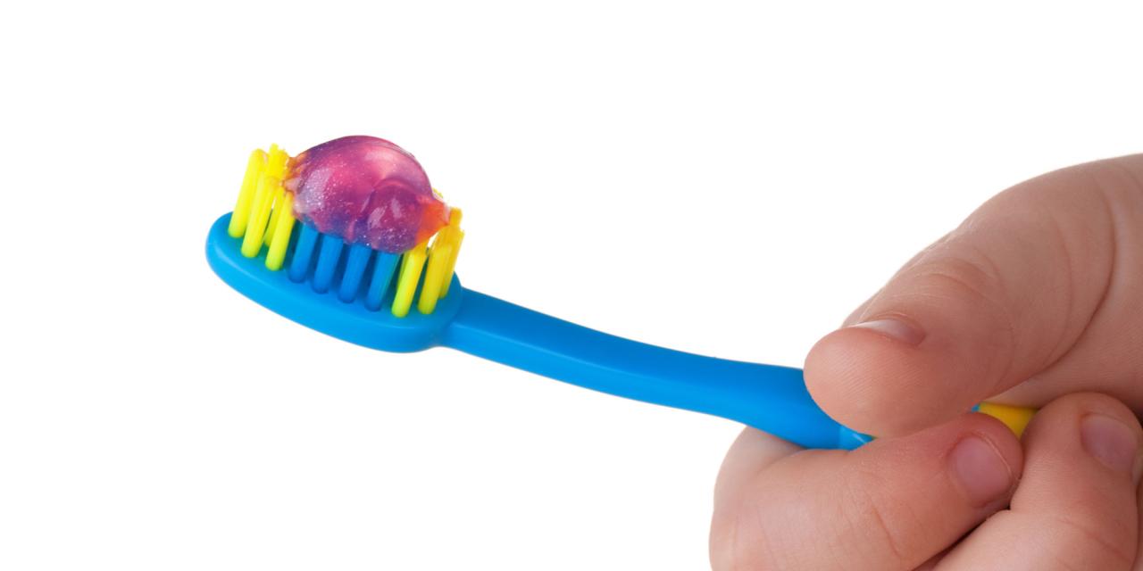 angeschnittene Kinderhand mit bunter Zahnbürste mit Pasta darauf