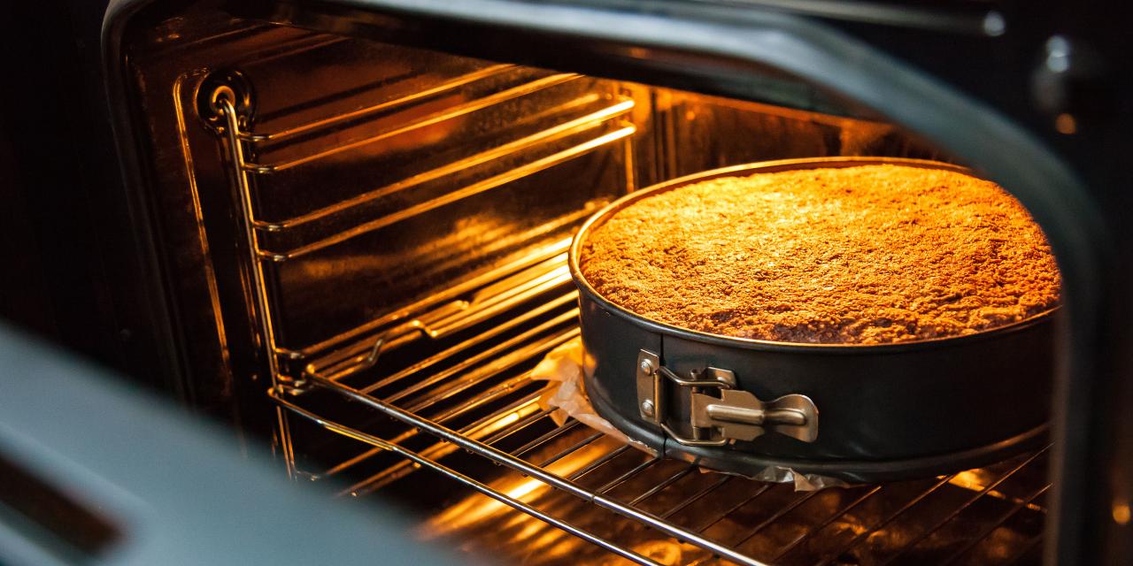 Blick in ein geöffnetes Backrohr. Darin steht eine Springform mit einem goldbraun gebackenen Kuchen.