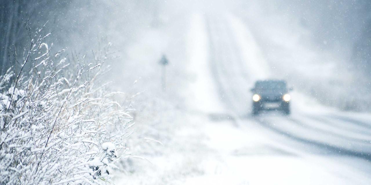Einsames Auto auf Landstraße bei Schneetreiben im Winter