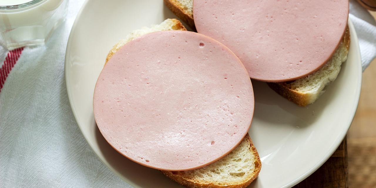 Kalbspariser auf zwei aufgeschnittenen Broten, die auf Teller liegen, dieser steht am Tisch