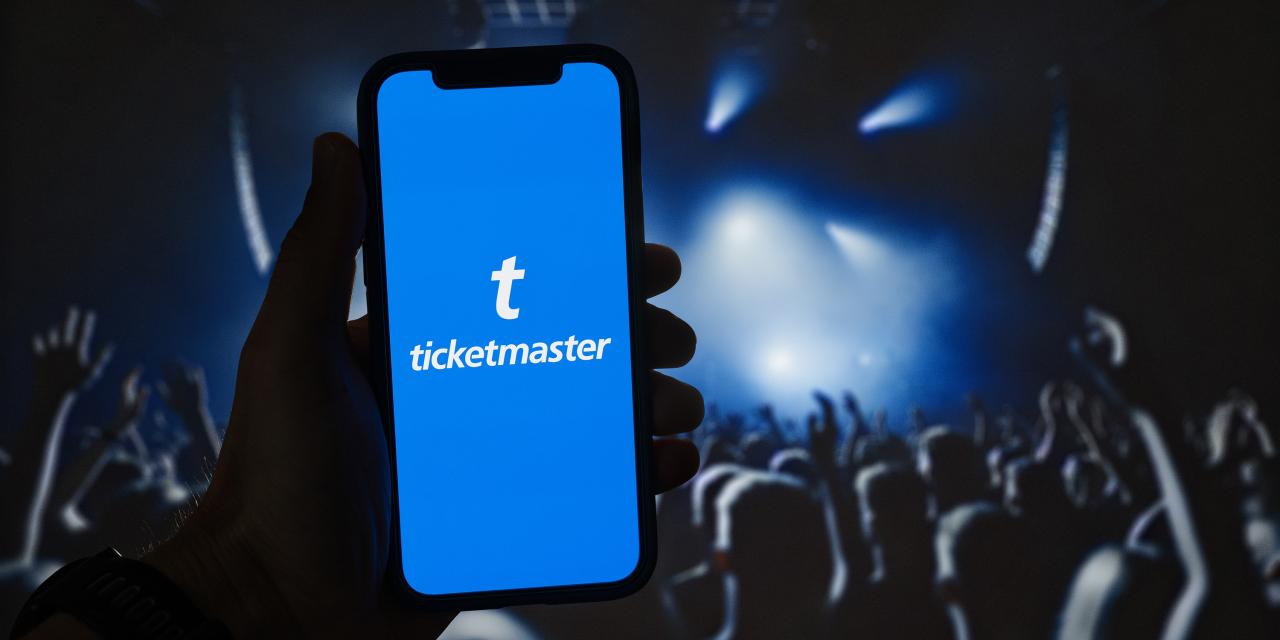 „Eine Person hält ein Smartphone mit der Ticketmaster-App auf dem Bildschirm. Im Hintergrund ist unscharf ein Konzert mit Bühne, Lichtstrahlen und jubelndem Publikum zu sehen.