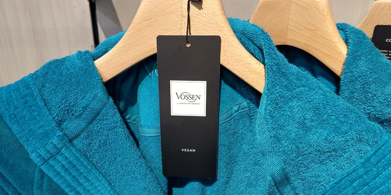 Blauer Bademantel am Kleiderbügel, am Etikett steht Vossen und vegan