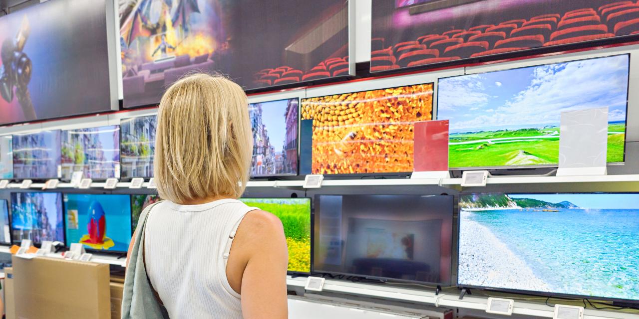 Eine Person steht im Ausstellungsraum eines Elektronikmarktes und betrachtet die Vielzahl an ausgestellten Fernsehern