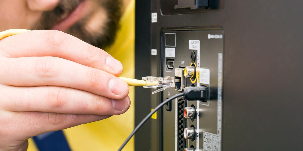 Ein bärtiger Mann schließt ein Internetkabel an einen Fernseher an. Man sieht die Rückseite des Gerätes mit diversen Anschlussmöglichkeiten.