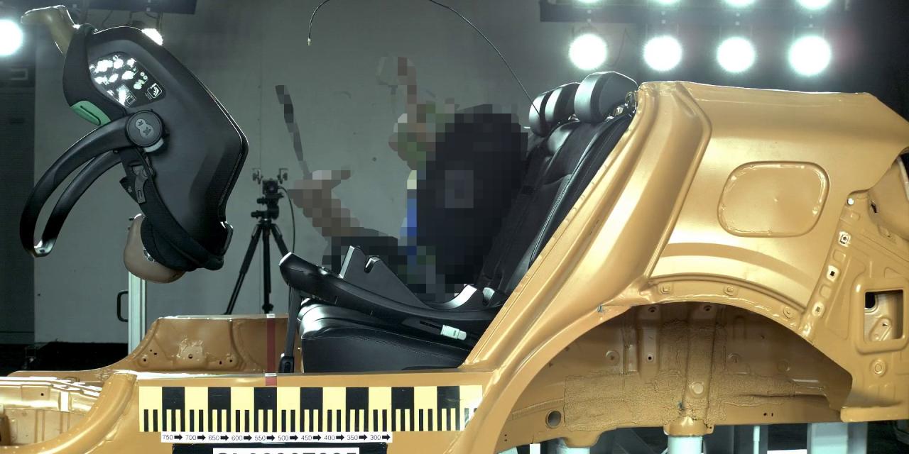 seitliche Ansicht einer Crash-Test-Situation, in der es einen schwarzen Autokindersitz noch vorne wegschleudert