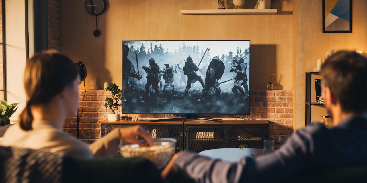 Ein jüngeres Paar sitzt auf der Wohnzimmercouch vor dem Fernseher und schaut einen Ritterfilm