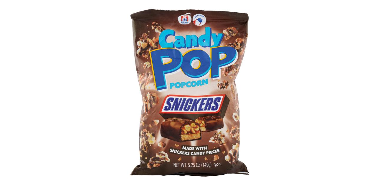 „Candy Pop Popcorn" in der Sorte „Snickers", brauner Beutel mit Popcornstücken und einem aufgeschnittenen Snickers-Riegel. Aufschriften „Made with Snickers candy pieces", „150 Calories" und „low sodium". Nettofüllmenge 149 Gramm.