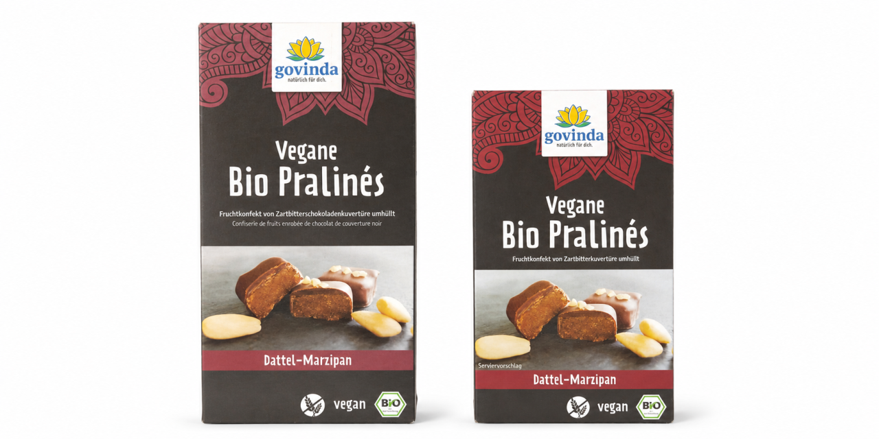 „Govinda" Vegane Bio Pralinés „Dattel-Marzipan" in zwei unterschiedlich großen Schachteln nebeneinander, links die größere, rechts die kleinere. Aufschrift links „Fruchtkonfekt von Zartbitterschokoladenkuvertüre umhüllt", rechts „Fruchtkonfekt von Zartbitterkuvertüre umhüllt".