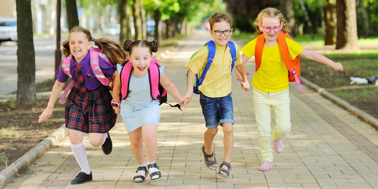 Vier Volksschulkinder mit bunten Rucksäcken laufend