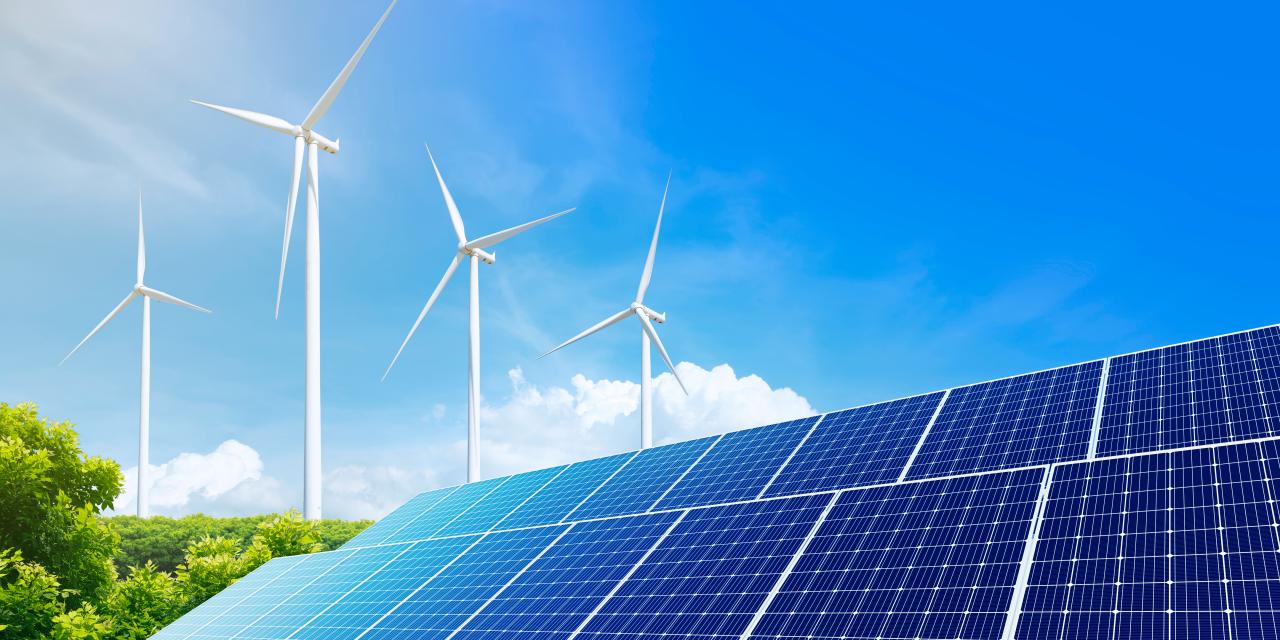 Solaranlage mit zahlreichen Photovoltaikmodulen und mehreren Windrädern vor blauem Himmel.