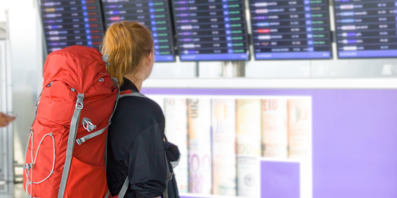 Junge Rucksacktouristin betrachtet Abfluganzeige am Flughafen