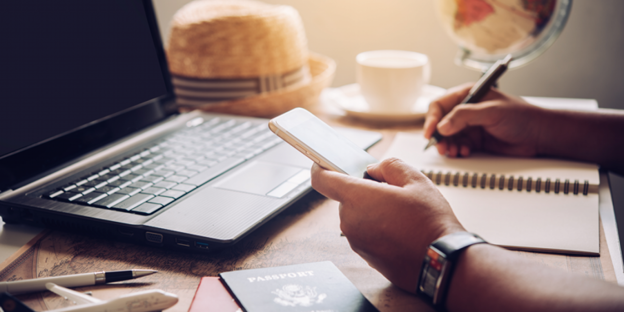 Mann am Laptop mit Smartphone in der Hand macht Notizen