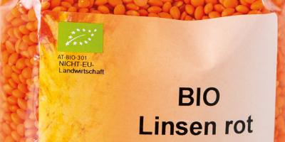 Teil einer Packung mit roten Bio Linsen. Verpackung ist durchsichtig. Produktbezeichnung steht auf weißem Schild