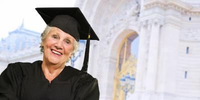 Weiterbildung im Alter: ältere Dame im Absolventenoutfit vor Universität