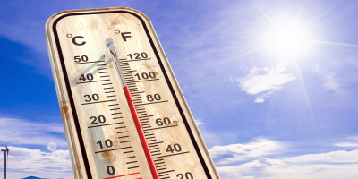 Ein Thermometer, das eine hohe Temperatur anzeigt. Dahinter Sonnenschein.