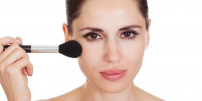 Frau trägt mit einem Kosmetikpinsel Make-up auf der Wange auf, Nahaufnahme