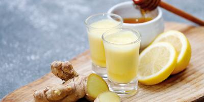 Ingwer-Shots auf einem Holzbrett mit Honig Zitronenscheiben und Ingwerknolle