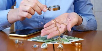 Ein Pfandleiher prüft mit einer Lupe den Wert von Ringen und einer Goldkette