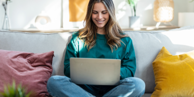 Eine junge Frau sitzt auf einem Sofa mit einem Laptop im Schoß.
