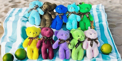 10 verschiedenfärbige Teddybären auf einer gestreiften Decke, die im Sand liegt