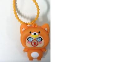 Auf dem Bild ist ein kleines, orangefarbenes Anhänger-Spielzeug zu sehen, das an einer gelben Perlenkette befestigt ist. Die Figur sieht aus wie ein niedliches Tier, vermutlich ein Fuchs, mit spitzen Ohren, großen Augen und roten Wangen. Auf dem Bauch befindet sich ein rundes Element mit bunten Symbolen. Die Figur hat einen weißen Bauch und kleine Füße. Der Hintergrund ist schlicht weiß, sodass der Anhänger deutlich im Mittelpunkt steht.
