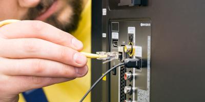 Ein bärtiger Mann schließt ein Internetkabel an einen Fernseher an. Man sieht die Rückseite des Gerätes mit diversen Anschlussmöglichkeiten.