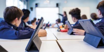 Eine Gruppe von Schülern sitzt in der Klasse und folgt dem Unterricht, die Tablets haben sie vor sich auf dem Tisch stehen.