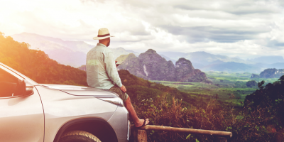 Man with hat leaning on the bonnet of a parked car and enjoying the distant view