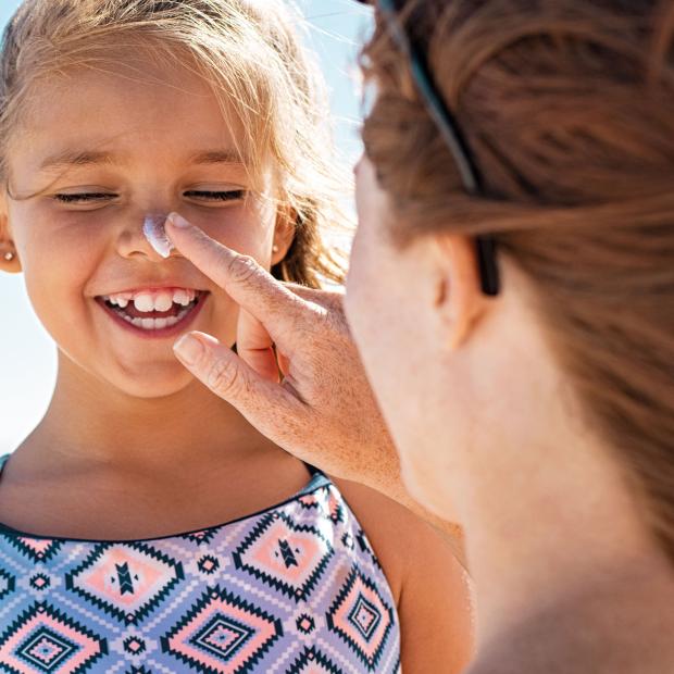 Frau cremt Gesicht von Kind mit Sonnencreme ein
