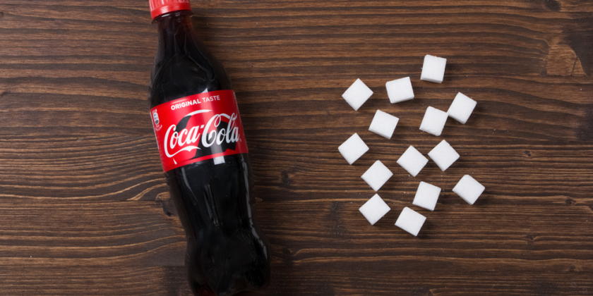 Coca Cola Flasche mit Zuckerwürfel vor Holzhintergrund