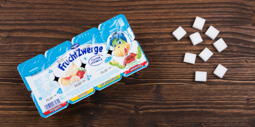 Fruchtzwerge-Joghurt mit Zuckerwürfel vor Holzhintergrund
