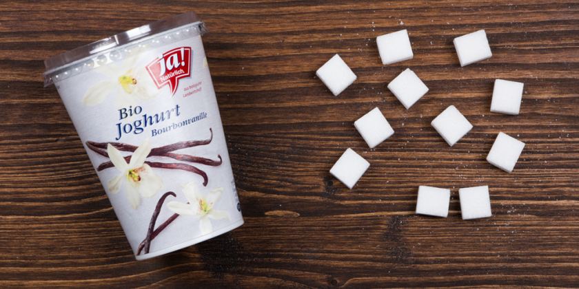 Vanillejoghurt mit Zuckerwürfel vor Holzhintergrund