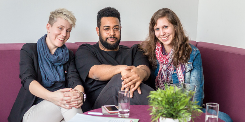 Drei Personen sitzen auf einer Couch.
