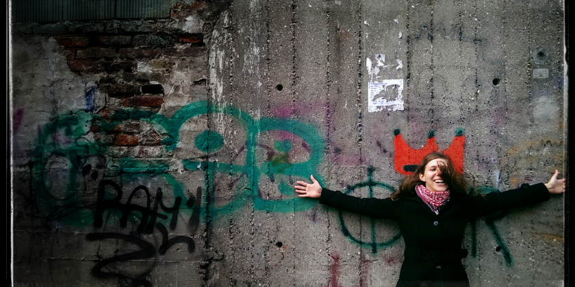 Frau vor Mauer, welche mit Graffiti beschmiert ist.