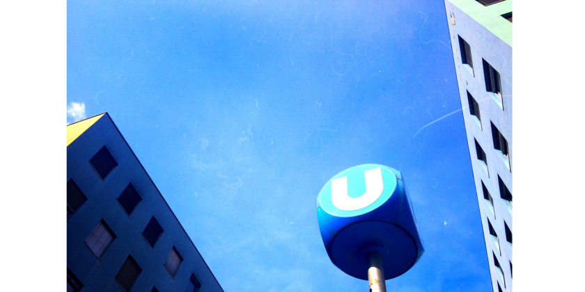 U-Bahn-Schild mit zwei Gebäudespitzen.