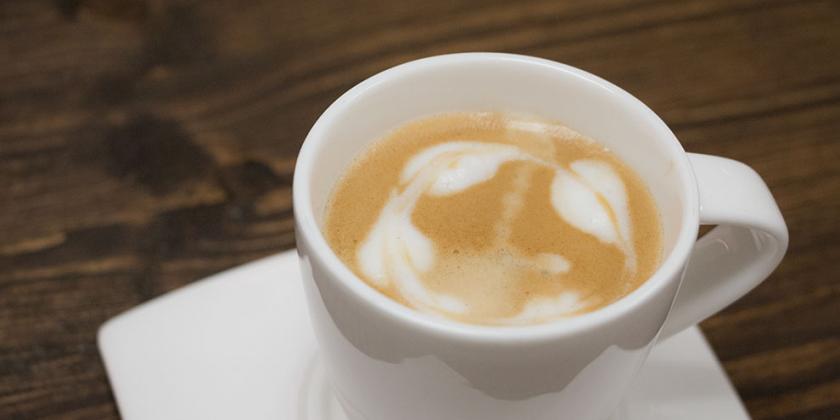 Latte Art: Kaffeetasse, Blättergirlande in Milchschaum gezeichnet.