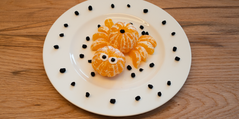 Geschälte Mandarine in Spinnenform mit Gesicht auf Teller